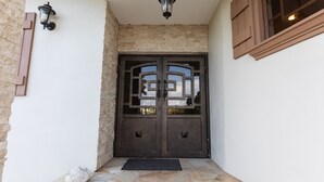 A stone-tiled entrance with a double door, a wall-mounted light fixture, and a wooden window frame. - Relax and enjoy breath taking ocean views from one of Tobago's premier villas! (Mount Irvine, Tobago)