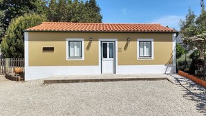 A two-story building with a beige facade and a red-tiled roof. There are two windows with white frames and a door with a white frame. The building is surrounded by gravel and has a pergola with chairs. - Family-friendly Cottage With Pool In Stunning Location (Alvorge)