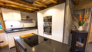 Een moderne keuken met een centraal eiland, inbouwovens en een houtkachel.