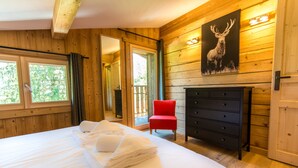 Een houten kamer met een bed, een rode stoel, een open haard en een schilderij van een hert.