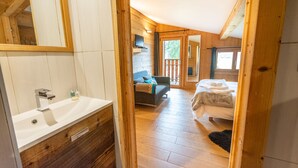 Een moderne badkamer met een groot wastafel en spiegel, een houten vloer en uitzicht op een slaapkamer met een bed en een bank.