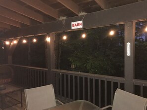 Un patio al aire libre con un letrero que dice 'BARN', terraza de madera y luces colgantes.