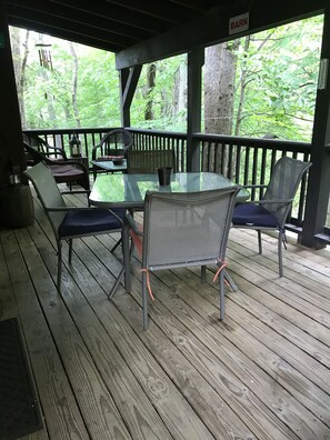 Un espacio de estar al aire libre cubierto con una mesa y sillas, rodeado por una terraza de madera y árboles.