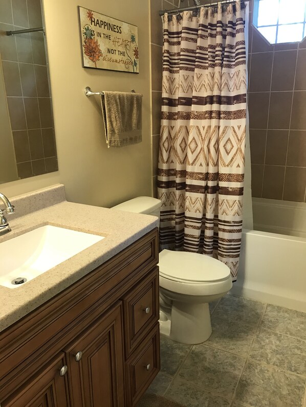 A bathroom with a white sink, wooden vanity, a toilet, and a shower curtain with a geometric pattern.