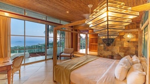 Quarto com uma cama grande, uma cadeira, uma escrivaninha e vista para o oceano.