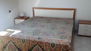 A bedroom with a patterned bedspread, a wooden headboard, a bedside table with a lamp, and a nightstand with a power outlet.