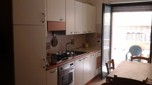 A kitchen with white cabinets, a stove, and a sink. There is a table and chairs outside the kitchen.