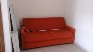 A red sofa in a corner of a room with white walls and a tiled floor.