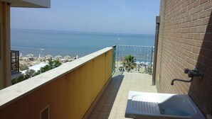 A balcony with a view of the sea, a small outdoor seating area, and a bathtub.