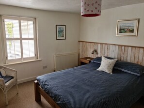A bedroom with a bed, a chair, a window with blinds, and two framed pictures on the wall. - Waterside Cottage In Emsworth, Hampshire (Emsworth)