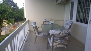 Un balcón con una mesa y cuatro sillas, un jarrón pequeño con flores y una ventana con rejas.