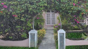 A stone pathway leading to a building with a white door, surrounded by lush greenery and flowering plants. - (1)Your Home away from Home with all the fun right at your finger tips (Rodney Bay)
