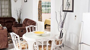 Ein Wohnzimmer mit einem braunen Sofa, einem weißen Esstisch mit Stühlen und einem weißen Kühlschrank.