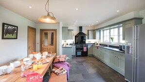 A spacious kitchen with a dining area, featuring a large wooden table set for breakfast, a built-in oven, and light-colored cabinets. - TIME - Charming Countryside Barn Conversion with Hot Tub & Scenic Views (Galashiels)