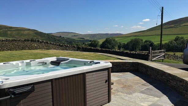 A hot tub with a stone wall backdrop, set in a stone-paved area with a view of rolling hills. - TIME - Charming Countryside Barn Conversion with Hot Tub & Scenic Views (Galashiels)