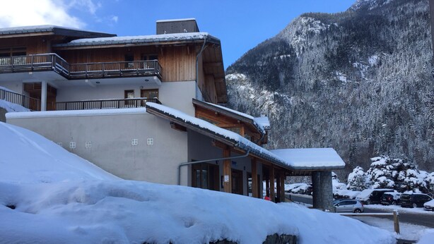 Un edificio de varios pisos con fachada de madera y un balcón, rodeado de montañas nevadas.