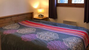 Un dormitorio con cama, una mesita de noche con lámpara, ventana con cortinas y vista a árboles.