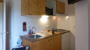 Una cocina compacta con armarios de madera, microondas, lavaplatos y fregadero.