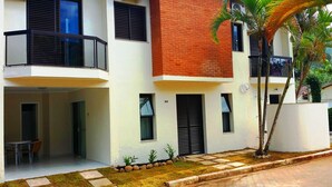 Un edificio residencial moderno de varios pisos con balcones, un pequeño jardín y una entrada pavimentada.