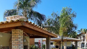 Un patio con una parrilla de ladrillo, rodeado de palmeras y un césped bien cuidado.