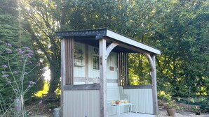 A small wooden structure with a covered porch, a table with chairs, and a potted plant. - Delightful House for Up to 6 Guests + Baby With Large Secluded Garden Area  (Fleury)