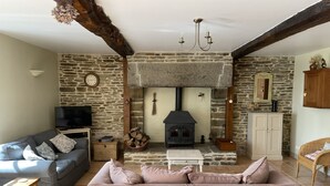 A cozy living room with a stone wall, a fireplace, a sofa, and a television. - Delightful House for Up to 6 Guests + Baby With Large Secluded Garden Area  (Fleury)