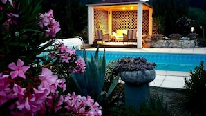Un gazebo con piscina e mobili da patio, immerso nel verde e tra fiori.