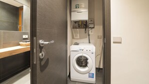 Un baño moderno y funcional con lavadora y secadora integradas, un perchero y un mueble de tocador de madera con una cesta.