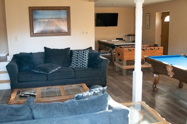 A living room with a dark-colored sofa, a pool table, and a foosball table.