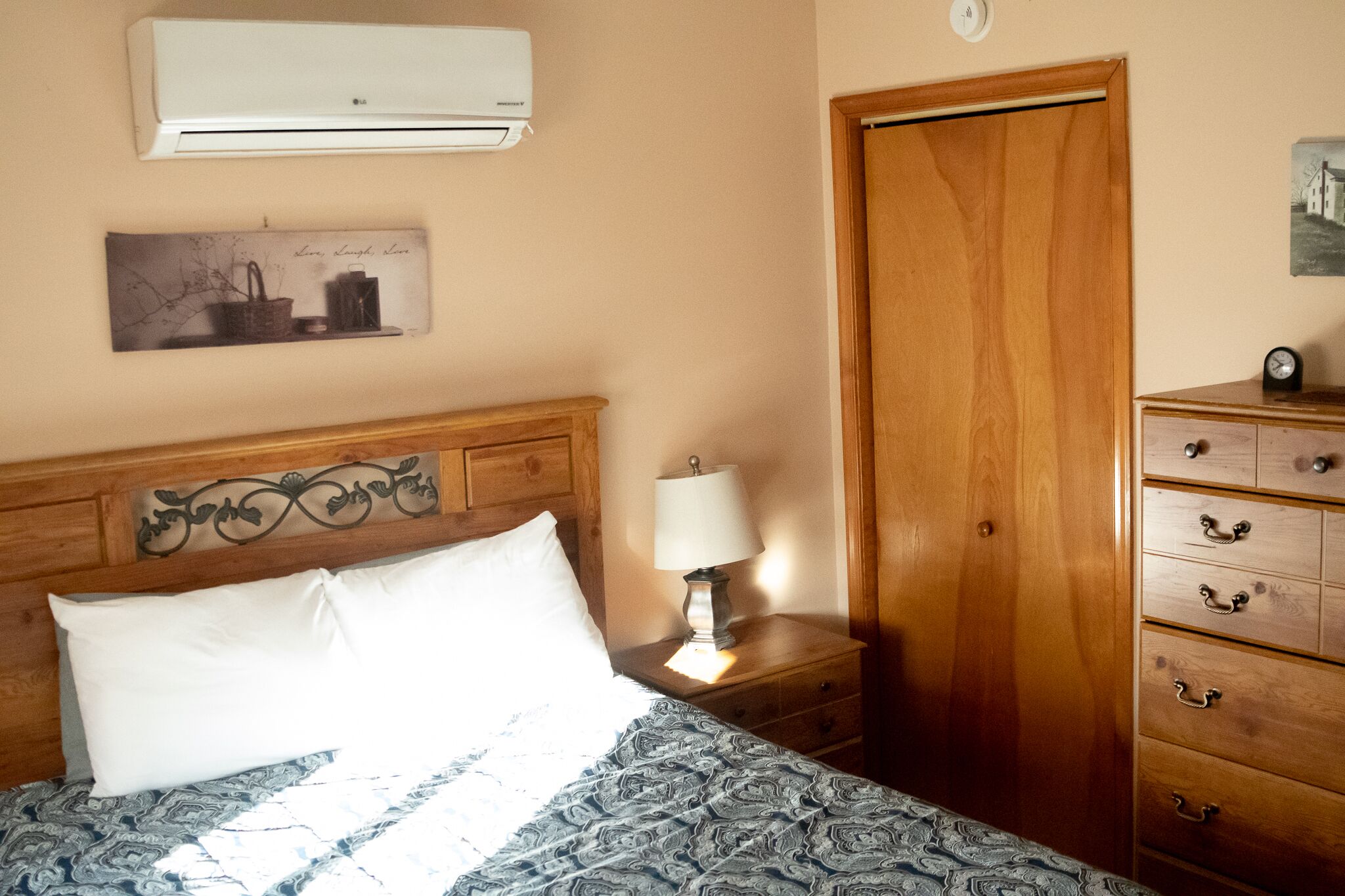 Ein Schlafzimmer mit Holz-Kopfteil, einer Nachttischlampe, einer Kommode mit Schubladen und einer Klimaanlage an der Wand.