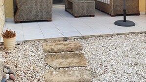 Un espace patio aménagé avec des meubles en osier, une table en verre et un grand parasol.