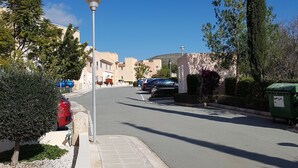 Une rue résidentielle bordée de voitures garées, avec un lampadaire et un grand arbre.