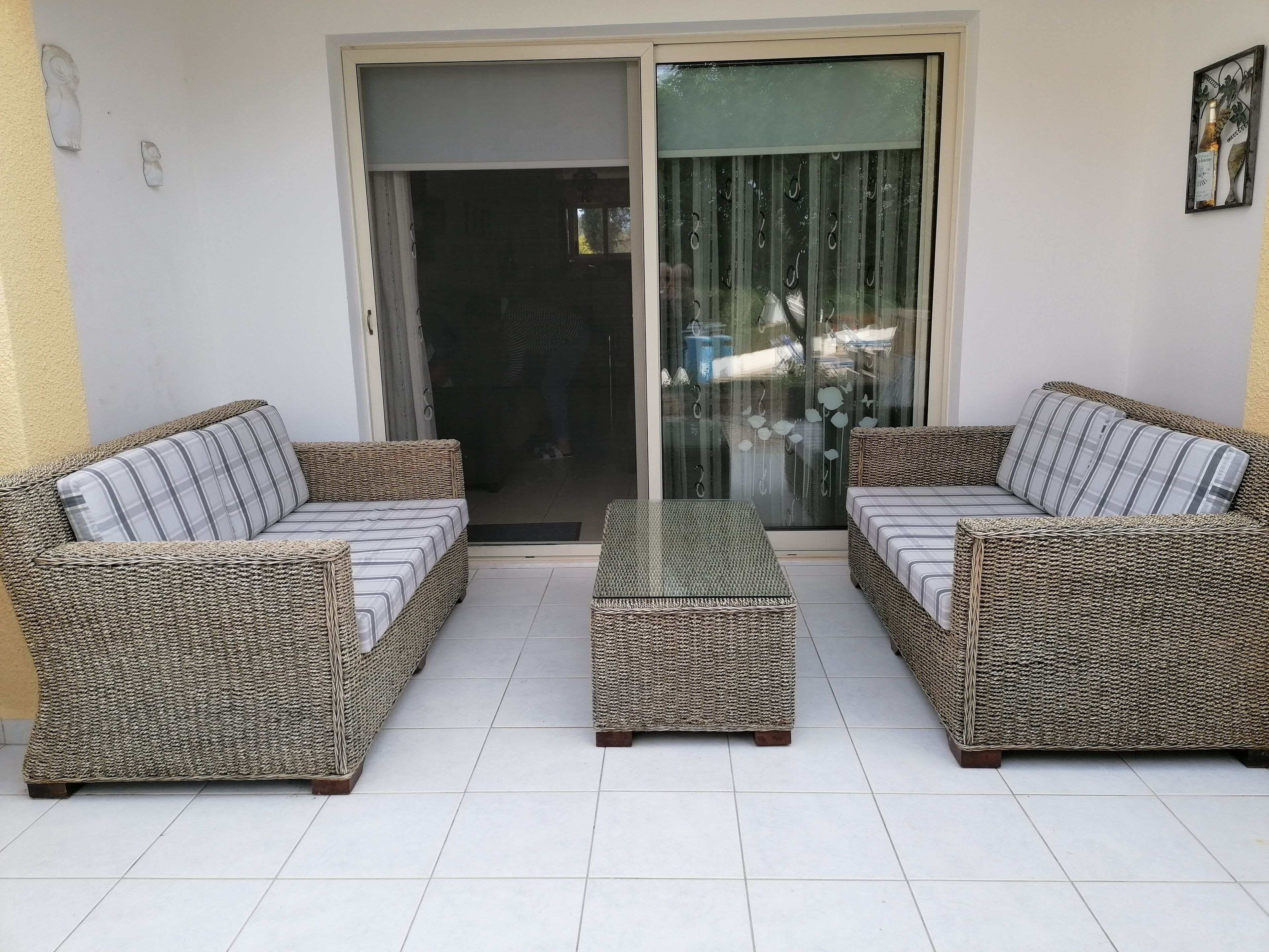 Un patio con dos sofás de mimbre y un reposapiés a juego, una mesa de vidrio y una puerta corrediza que da a un espacio interior.