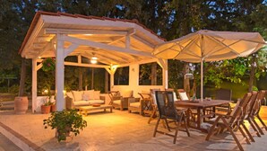 A covered outdoor seating area with a table and chairs, surrounded by potted plants and a pergola. - Villa Dora · Villa Dora (Faliraki)