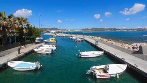 A marina with several small boats docked along a concrete pier, surrounded by calm water and palm trees. - Villa Dora · Villa Dora (Faliraki)