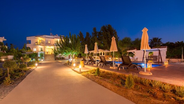 A well-lit outdoor area with a swimming pool, lounge chairs, and umbrellas. - Villa Dora · Villa Dora (Faliraki)