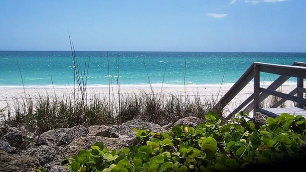 A beach with clear turquoise water, a wooden deck, and some greenery in the foreground. - Cottage within walking distance to Casey Key Beach (Nokomis)