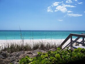 A beach with clear turquoise water, a wooden deck, and some greenery in the foreground. - Cottage within walking distance to Casey Key Beach (Nokomis)
