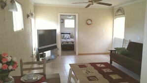 A living room with a TV, a sofa, a dining table with chairs, and a ceiling fan. - Cottage within walking distance to Casey Key Beach (Nokomis)