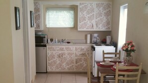 A compact kitchen with a dining area, featuring a tiled floor, a small refrigerator, a stove, and a dining table with chairs. - Cottage within walking distance to Casey Key Beach (Nokomis)