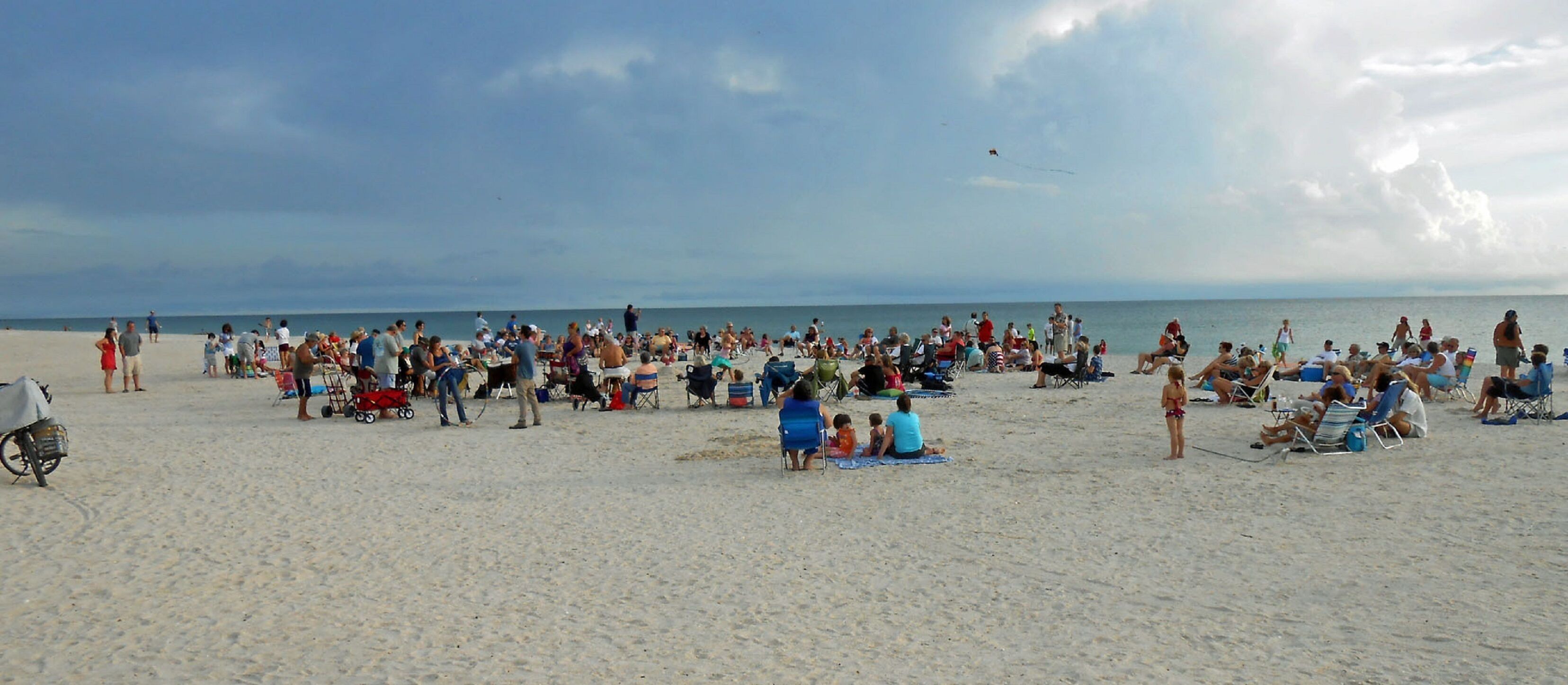 Une plage bondée, où les gens sont assis sur des chaises et des couvertures.