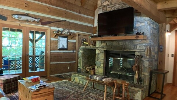 Ein gemütliches Blockhaus-Interieur mit Kamin aus Stein, Holzmöbeln und einem an der Wand befestigten Fernseher.