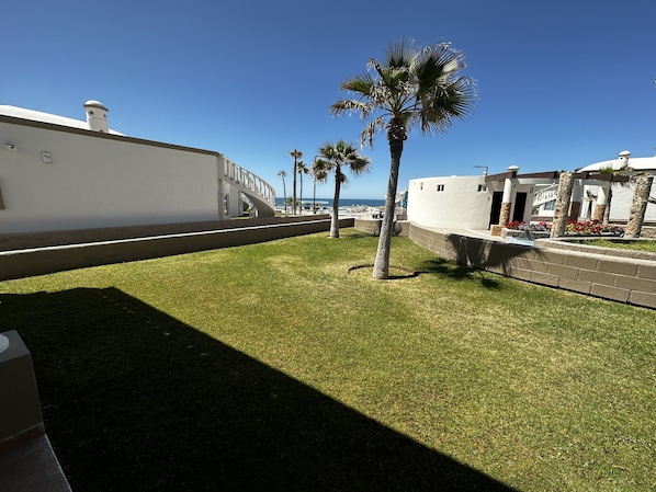 A courtyard with a white building, palm trees, and a view of the sea.