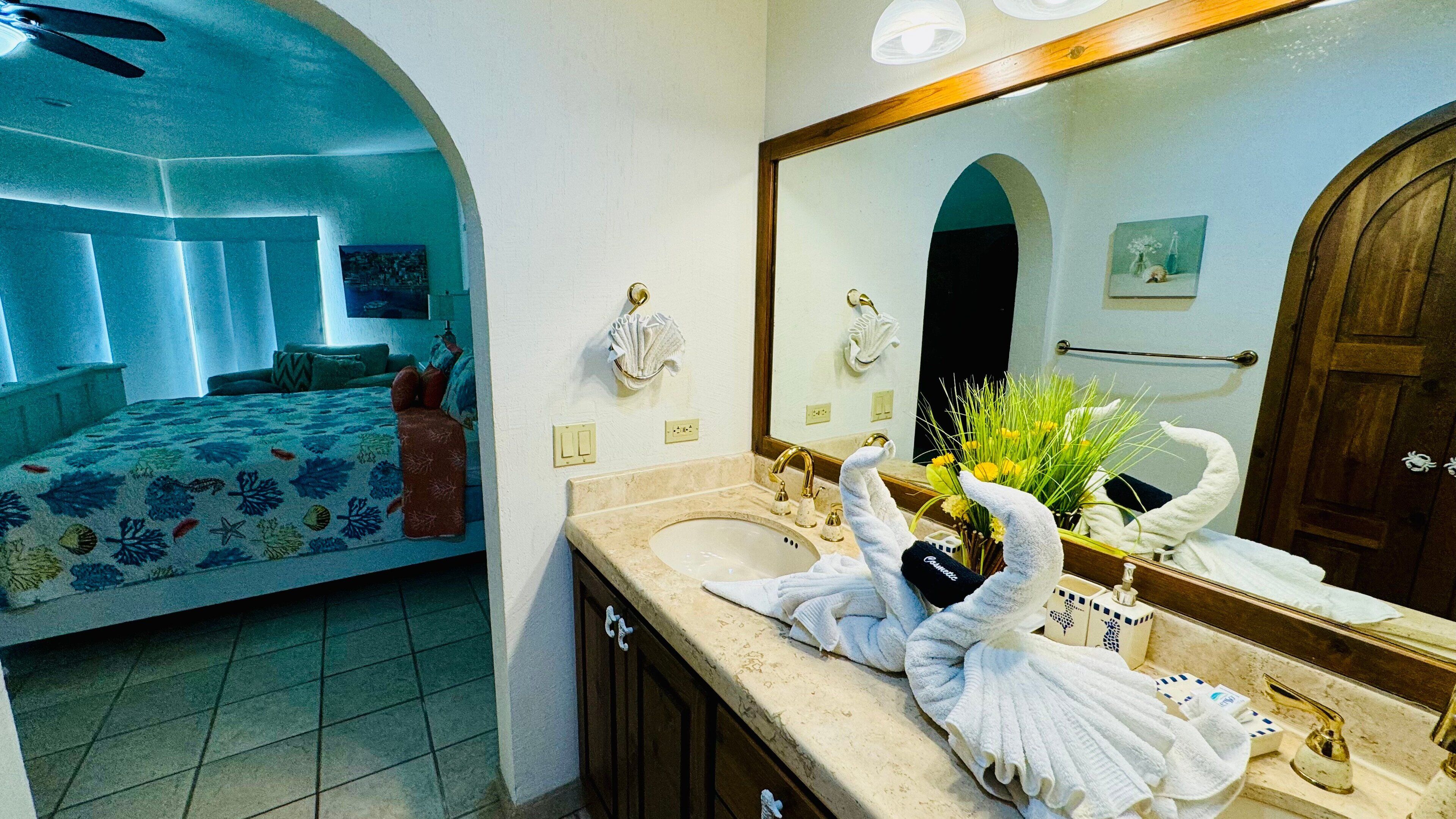 A hotel room with a bed, a bathroom with a sink, and a mirror.
