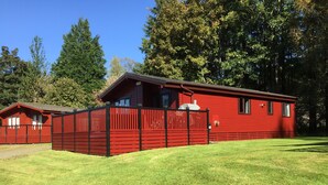 Una cabaña roja con un patio cercado, rodeada de árboles.