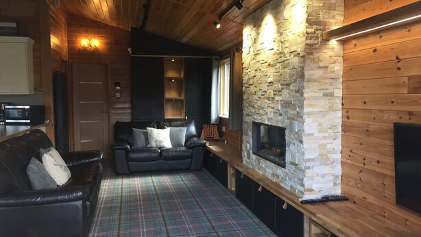 Una sala de estar acogedora con chimenea, paredes de madera, alfombra escocesa y un sofá de cuero.