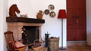 Une pièce chaleureuse avec une cheminée, un fauteuil à bascule, une porte rouge et une lampe.
