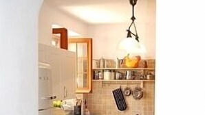 Une cuisine avec des armoires blanches, un plan de travail en bois et un luminaire suspendu.