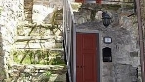 Un bâtiment en pierre avec une porte rouge et un petit balcon doté d’une rambarde en métal.