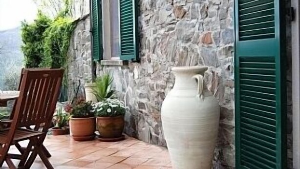 Un bâtiment en pierre avec des volets verts, une chaise en bois et des plantes en pot.